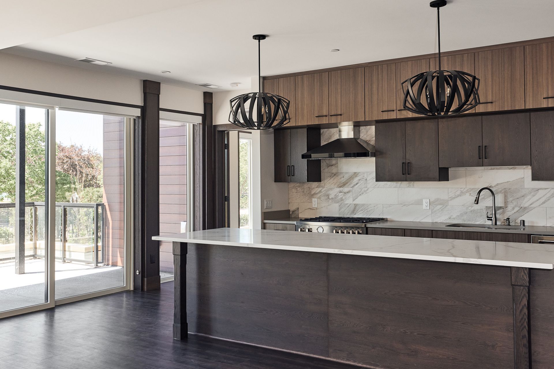 Modern kitchen with island, dark wood cabinetry, marble backsplash, and large windows.