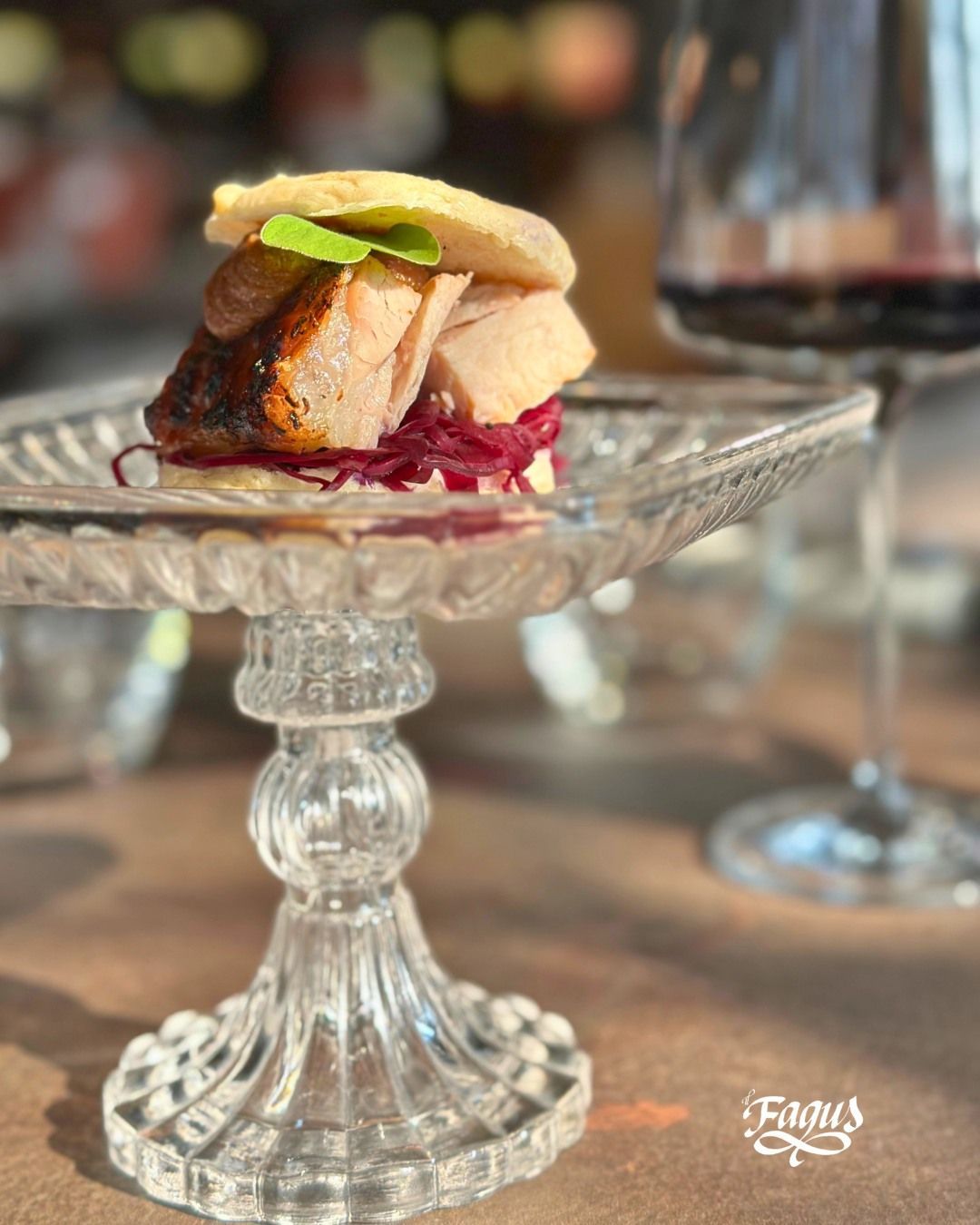 Un piatto di vetro con un panino sopra accanto a un bicchiere di vino.