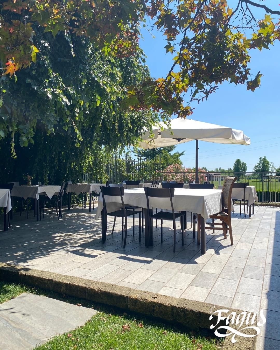 Un patio con tavoli e sedie sotto gli ombrelloni e un cartello che dice fagun