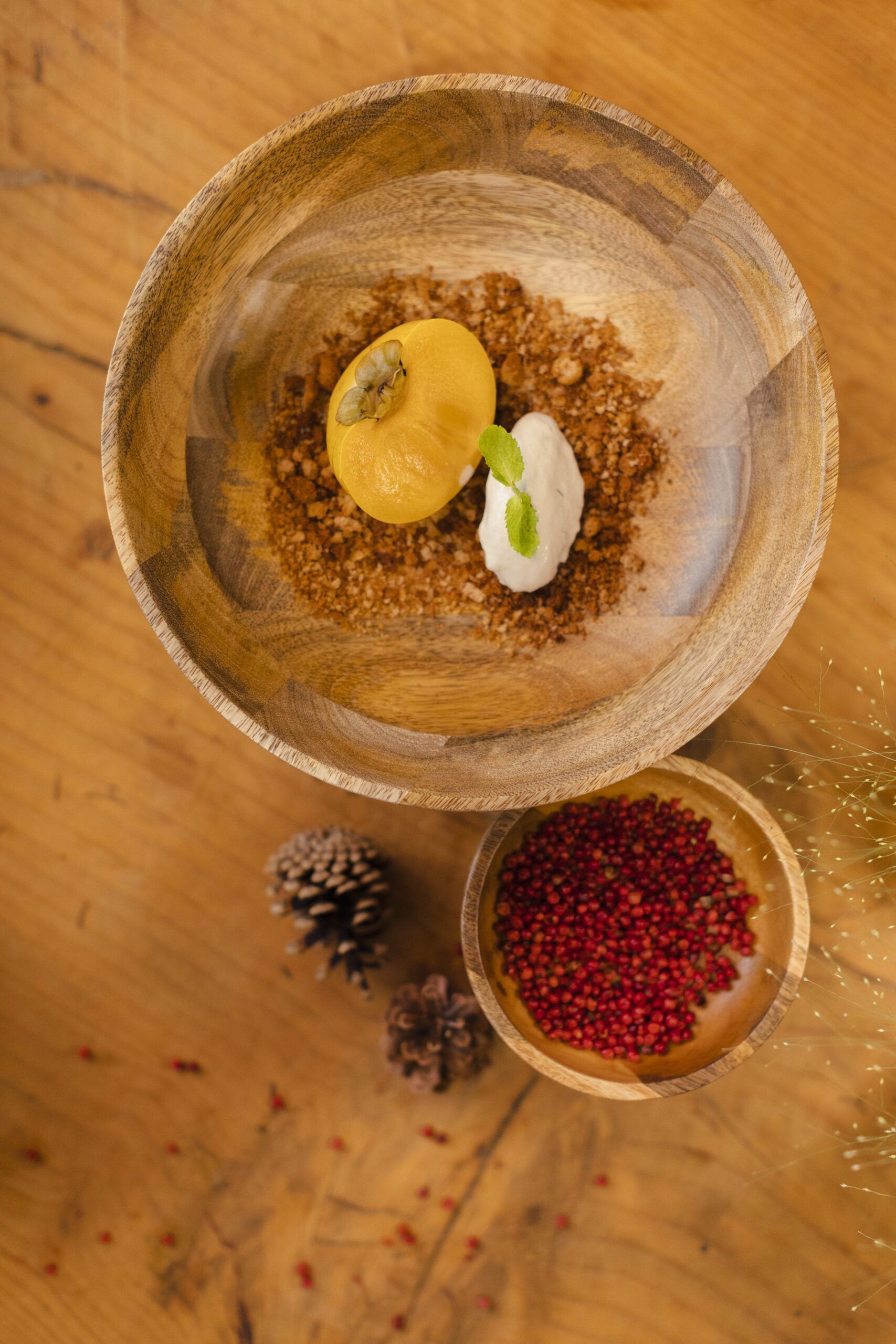 Una ciotola di legno piena di cibo e una ciotola di grani di pepe rosa su un tavolo di legno.