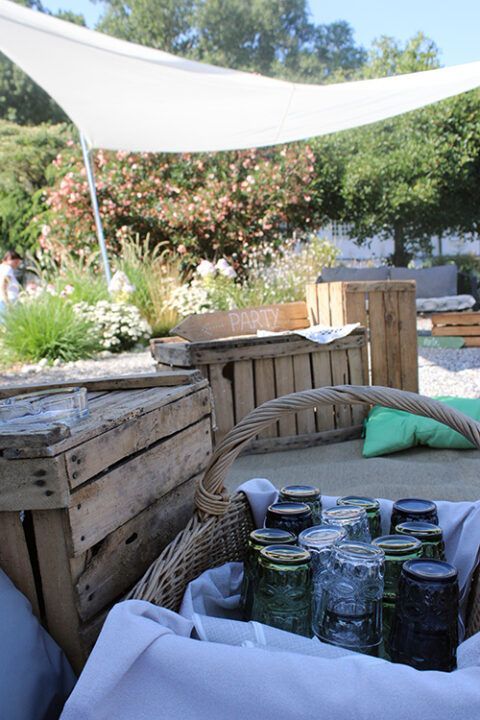 Un cesto pieno di barattoli e bicchieri è appoggiato sotto una vela bianca.