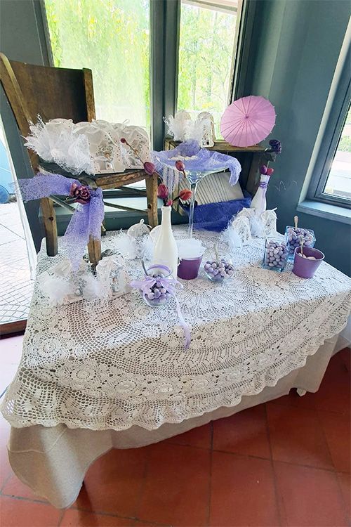 Un tavolo con una tovaglia di pizzo e decorazioni viola.