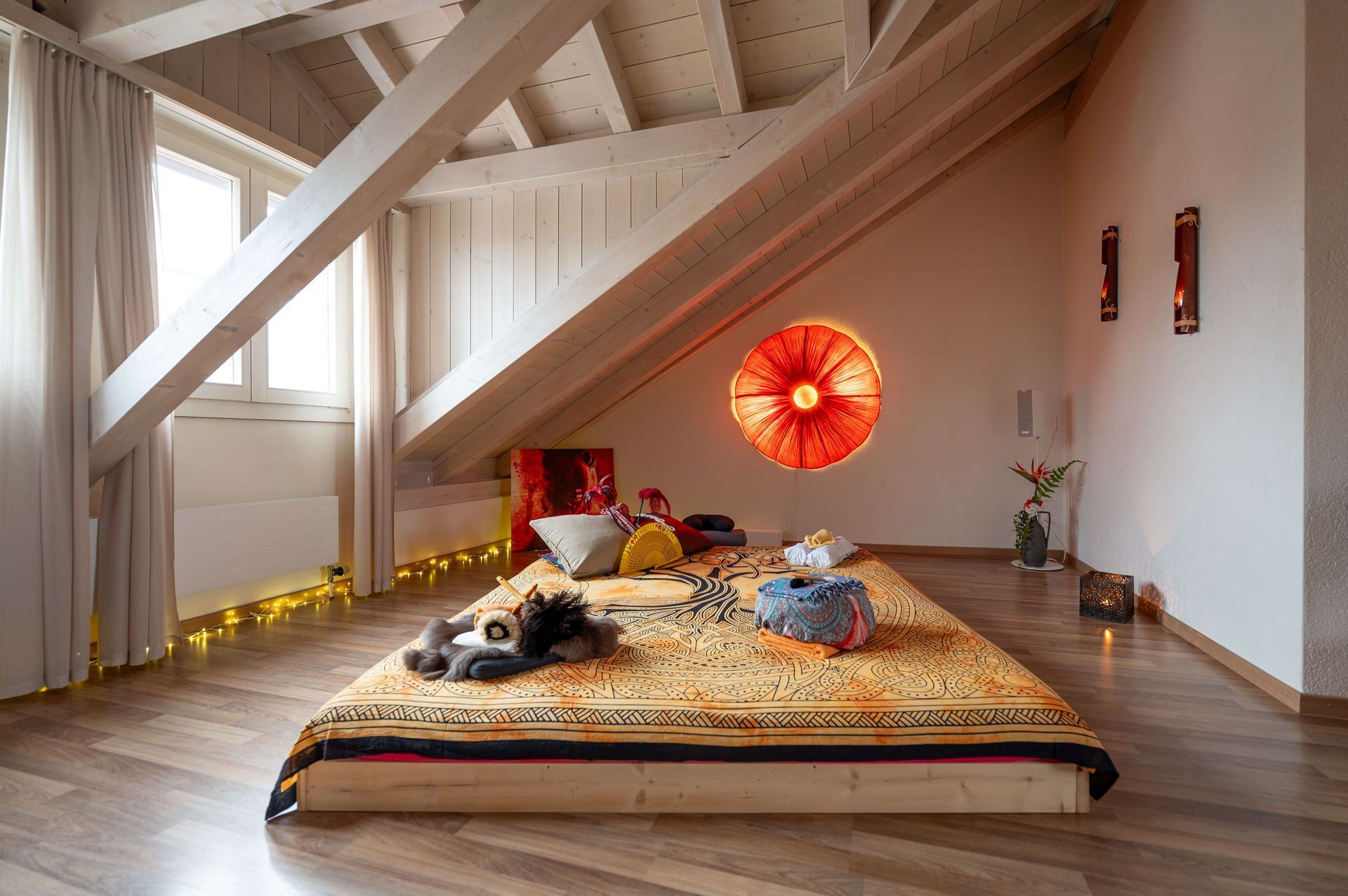 Weisses, gemütliches Dachzimmer mit stilvoller Lampe und einem grossen Futon in der Mitte.