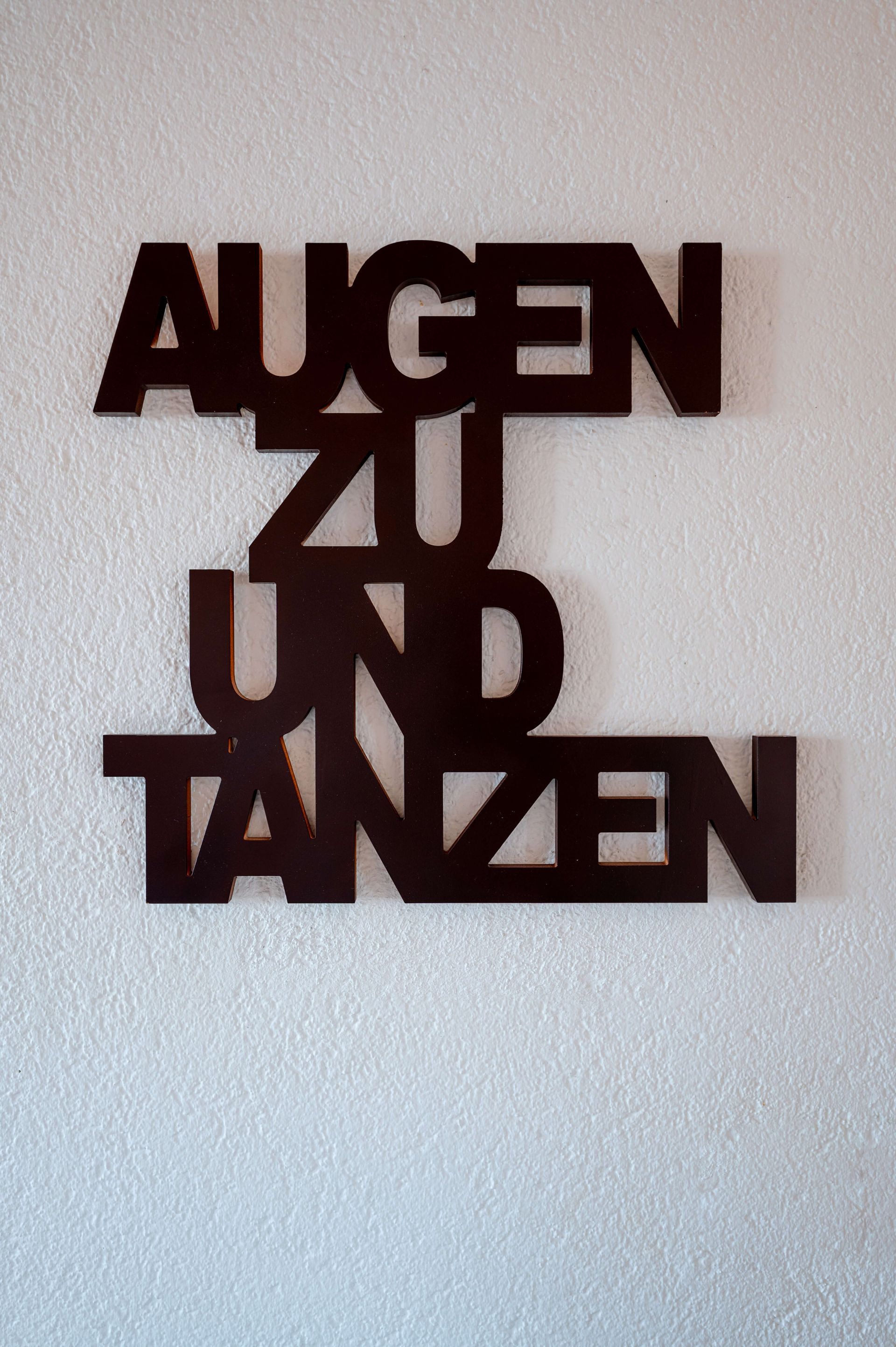 Schriftzug aus grossen Holzbuchstaben an einer weissen Wand mit den Worten Augen zu und Tanzen