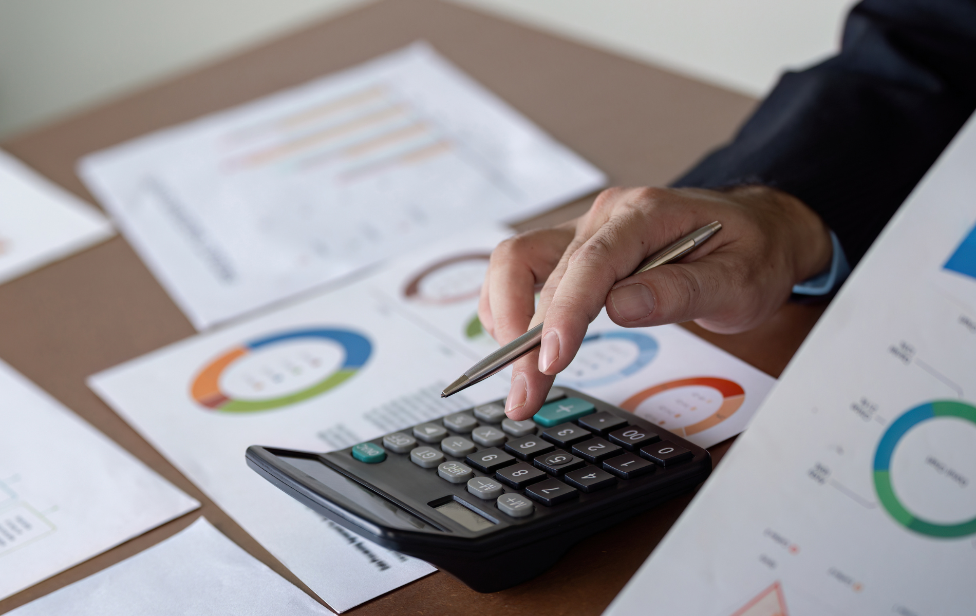 A person is using a calculator and pointing at it with a pen.