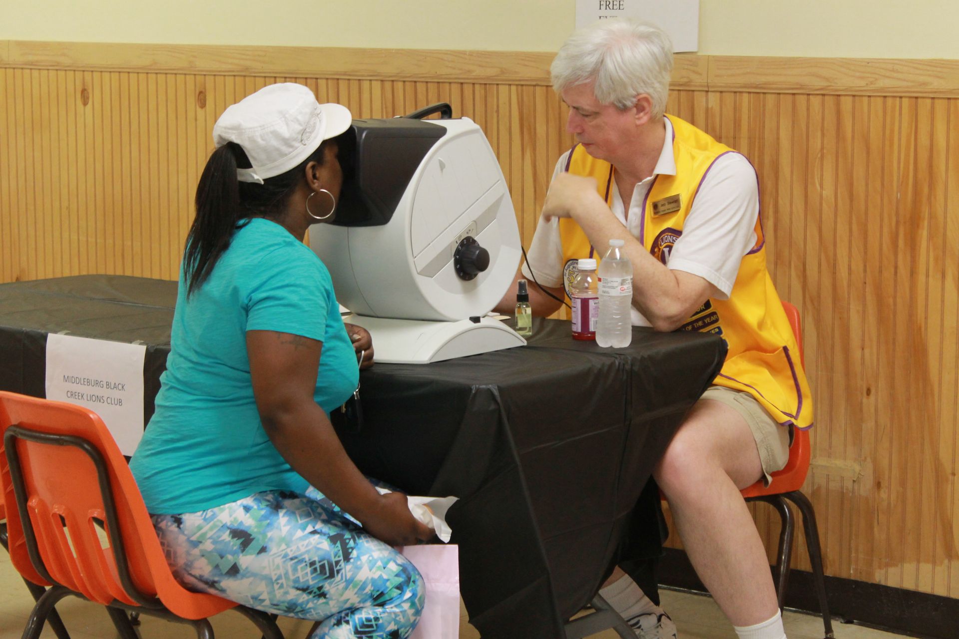 Woman getting eye exam at a clinic by a man wearing a yellow vest.
