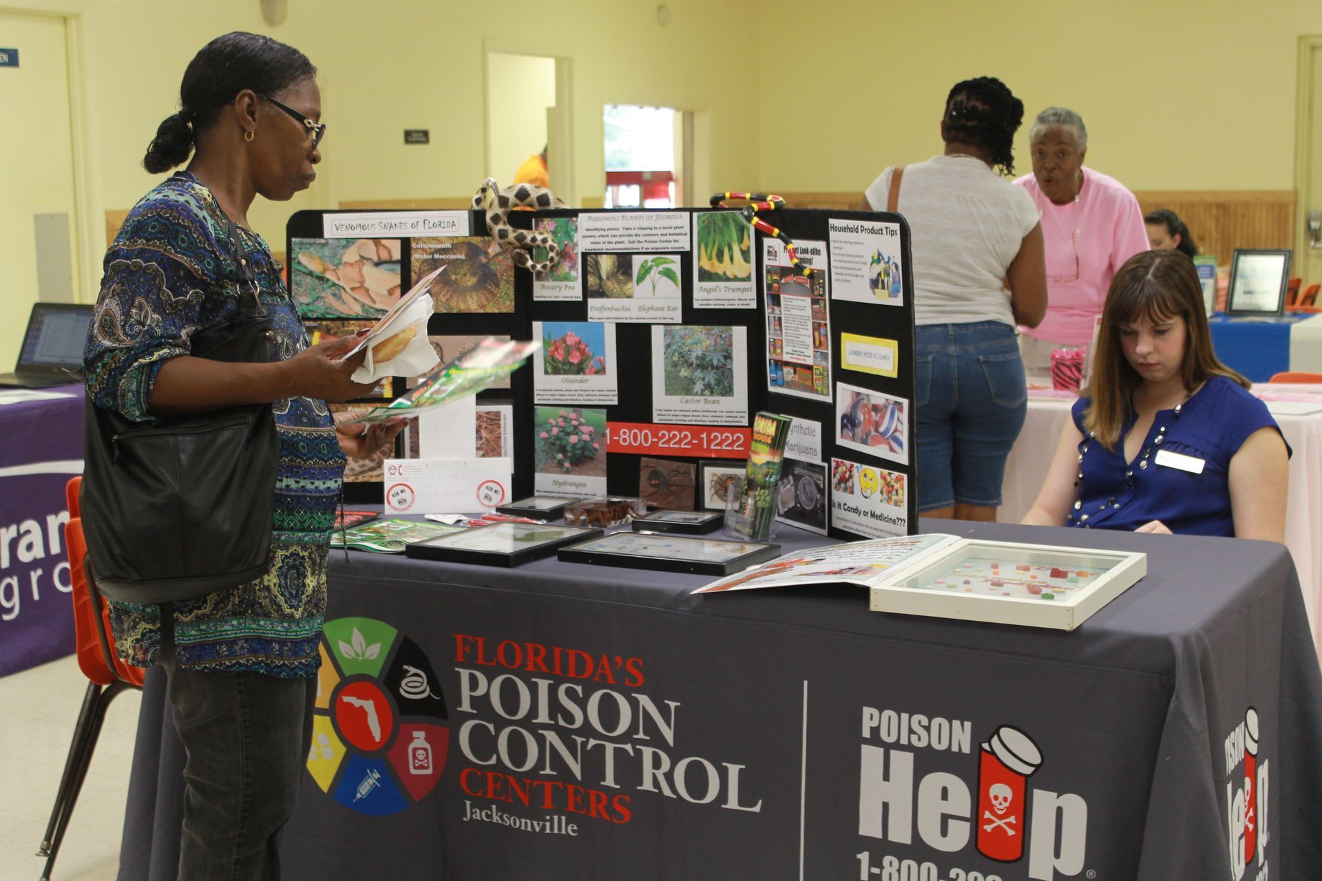 Woman at a Florida Poison Control Centers information booth, examining materials. Others browse nearby.