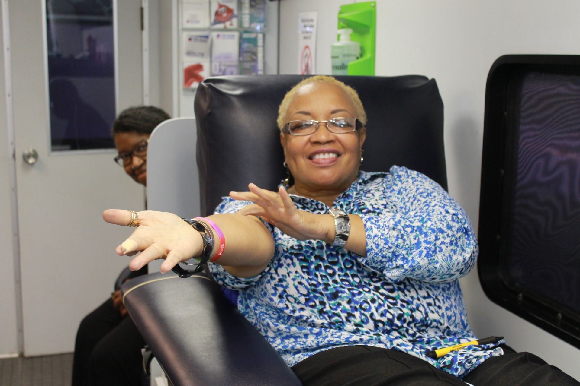 Woman in blue shirt with bandaged arm, smiling while donating blood.