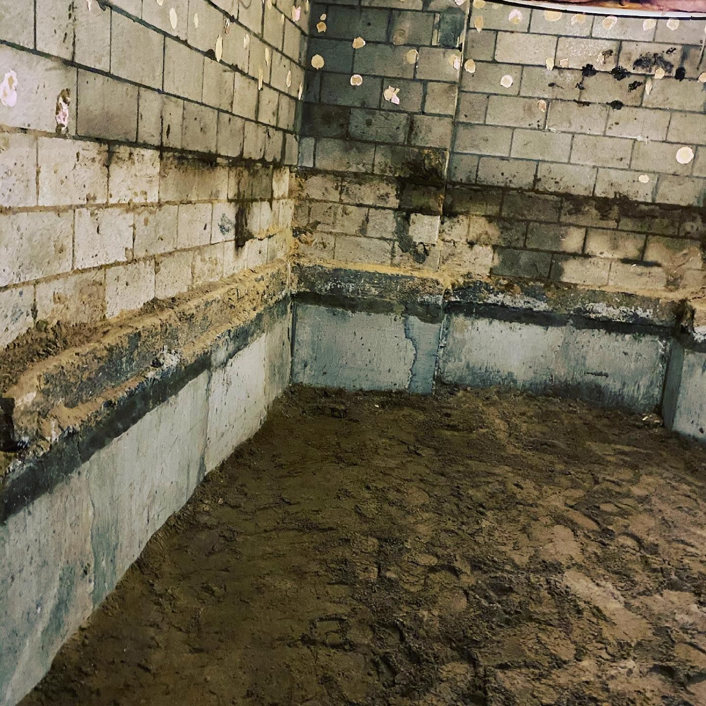 A dirty room with a brick wall and a dirt floor