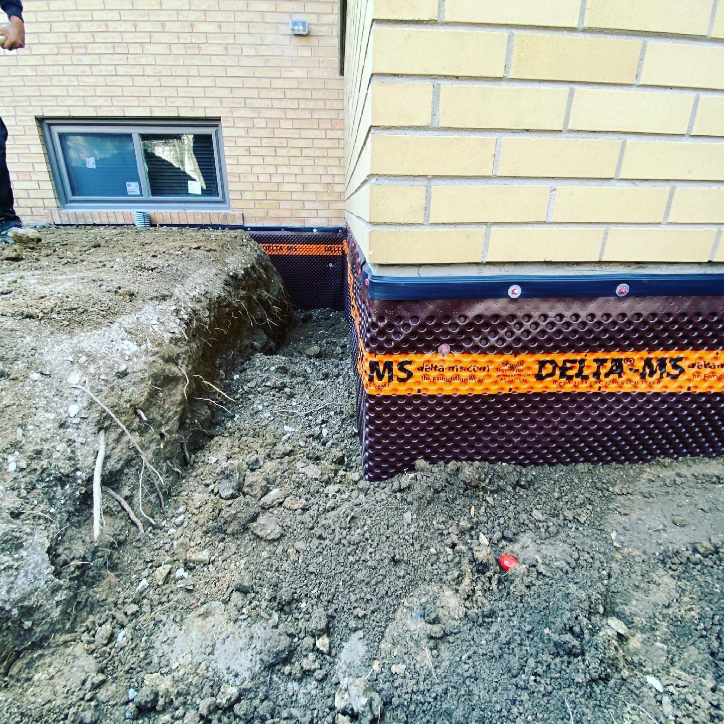 A man is digging a hole in front of a brick building.