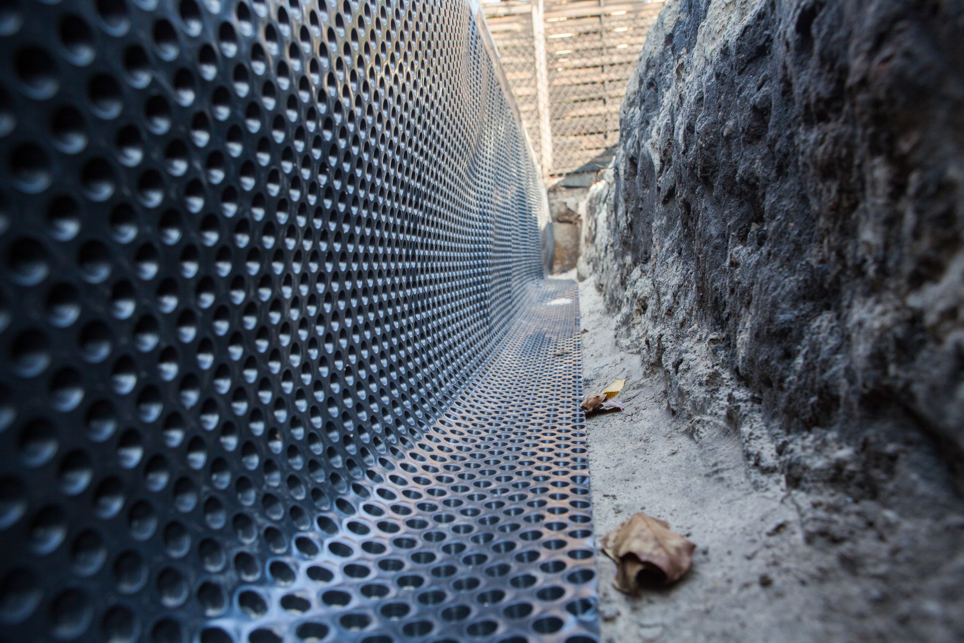 Black dimpled drainage membrane lining a foundation wall.
