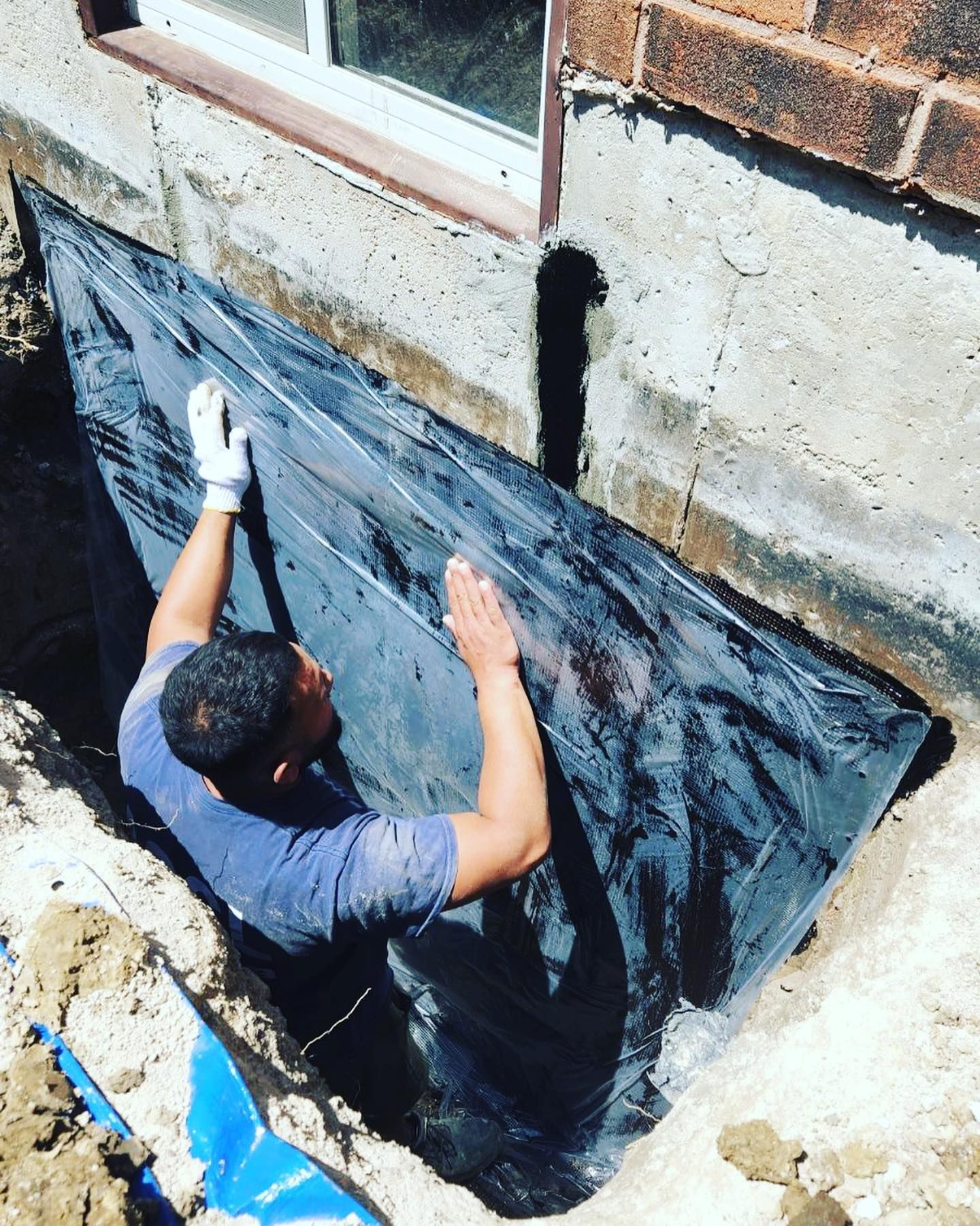 A man is laying a black tarp on a brick wall.