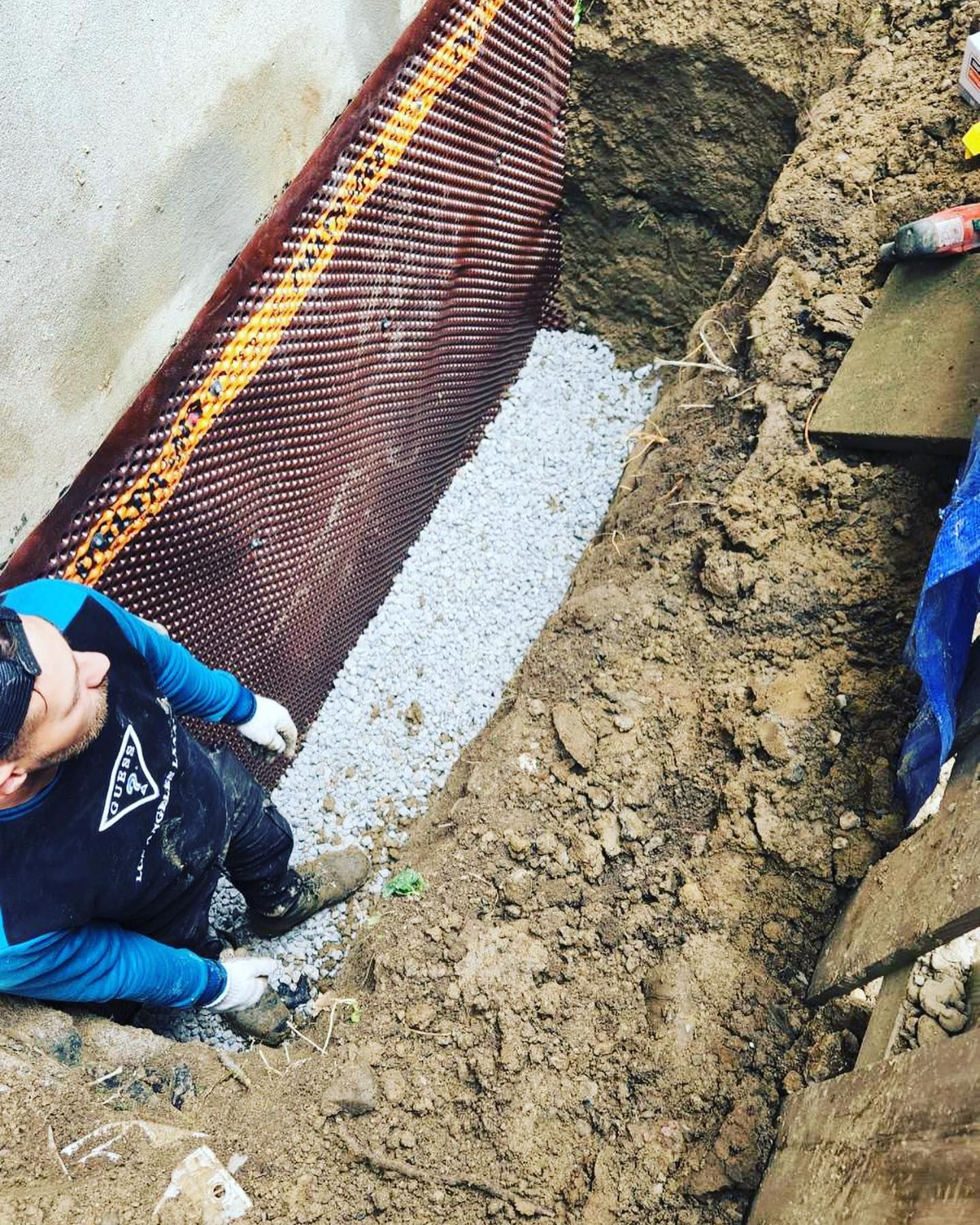 A man is kneeling in the dirt next to a wall.