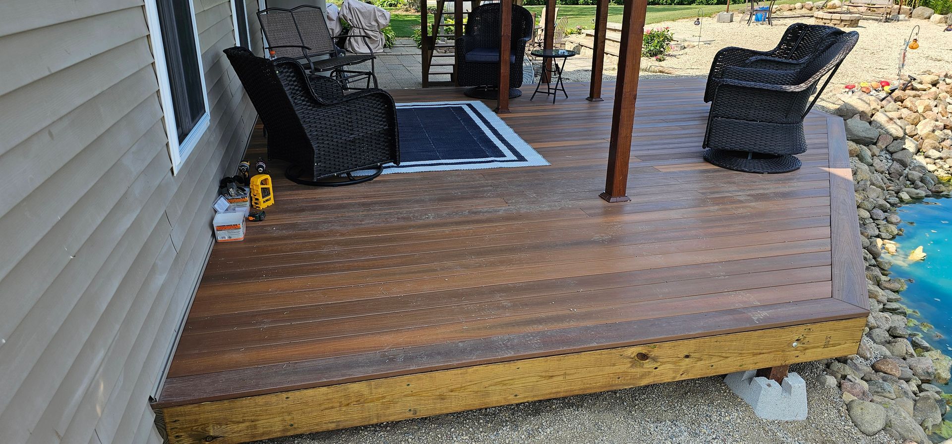 People installing wooden deck boards beside a tree, using a drill and gloves