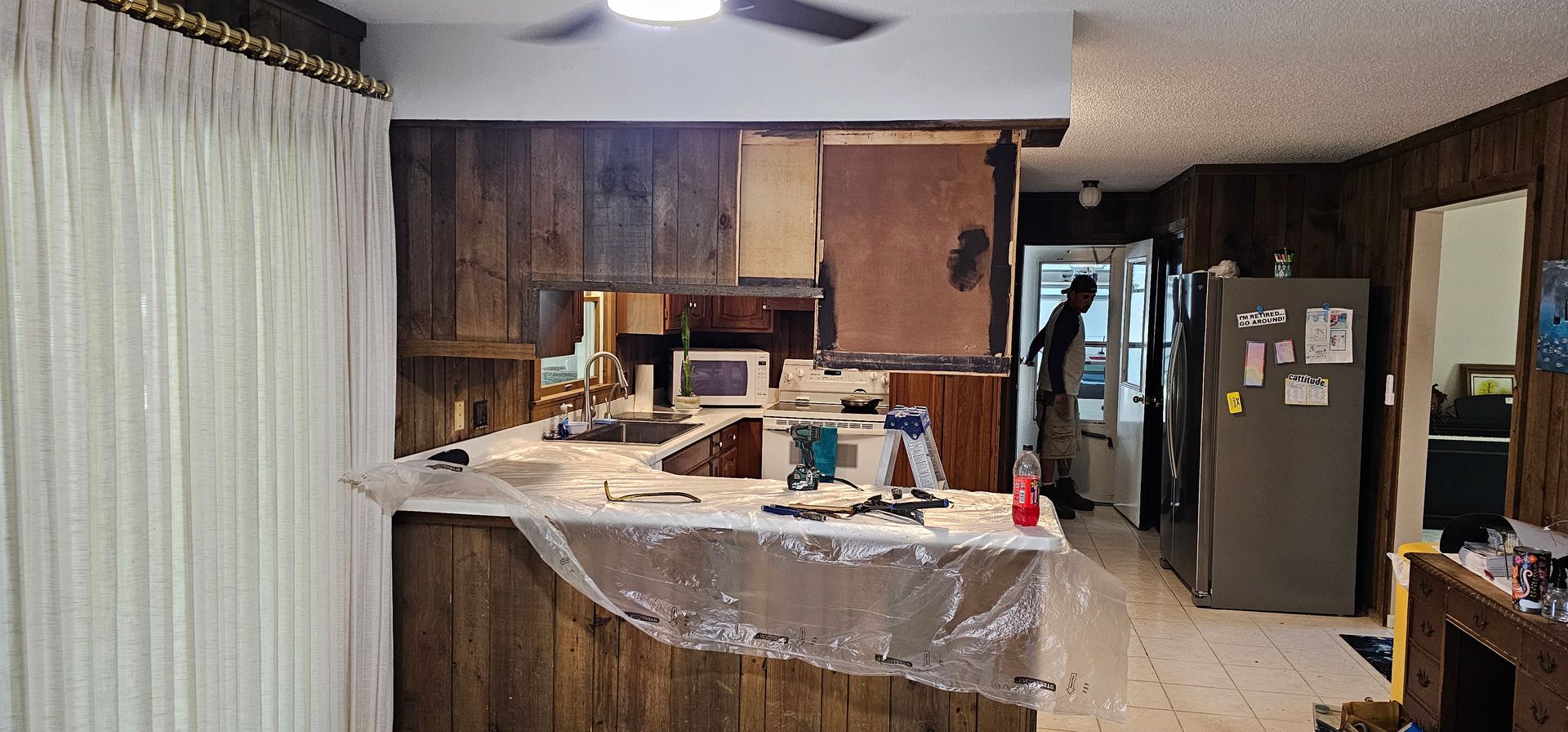 Modern kitchen with dark wood cabinets, white countertops, stainless steel appliances, and light tile flooring