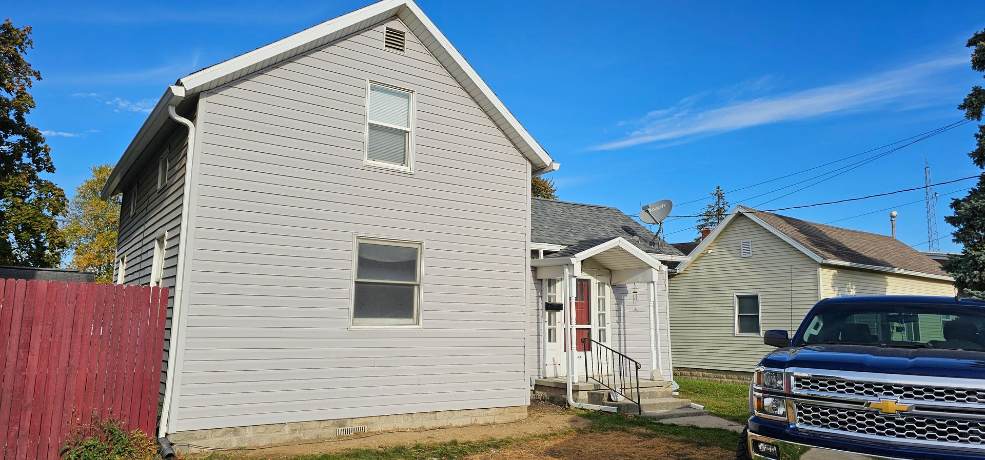 Yellow house exterior with dark trim and multiple windows against a cloudy sky