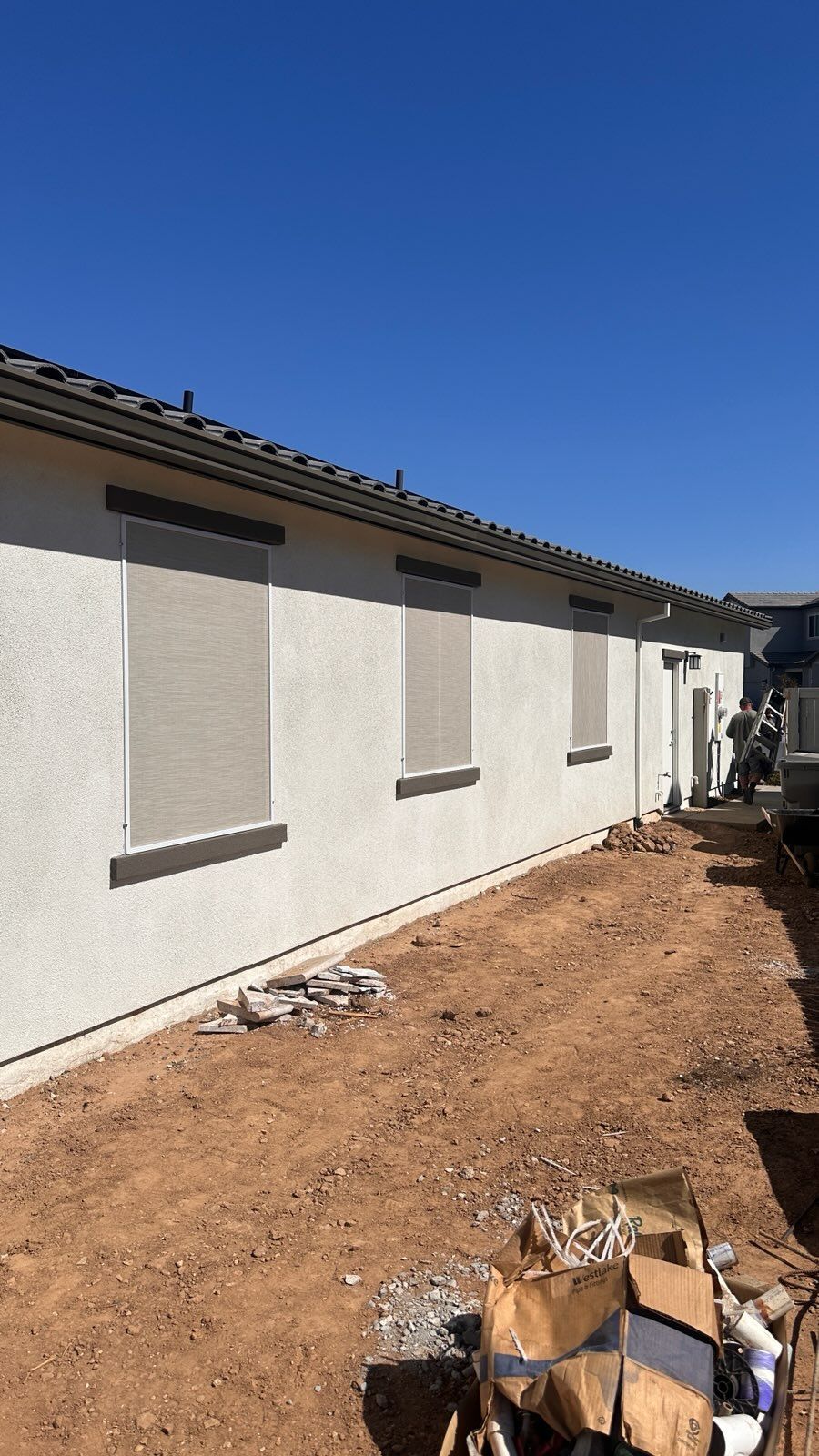 A white house with a lot of windows is sitting on top of a dirt field.