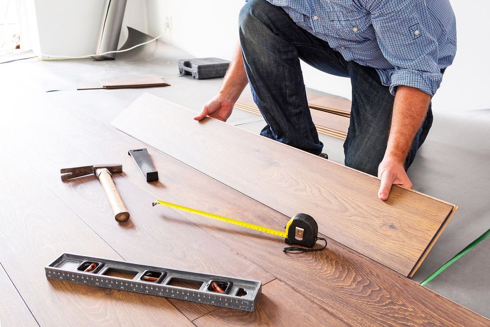 A man is kneeling down to install a wooden floor.