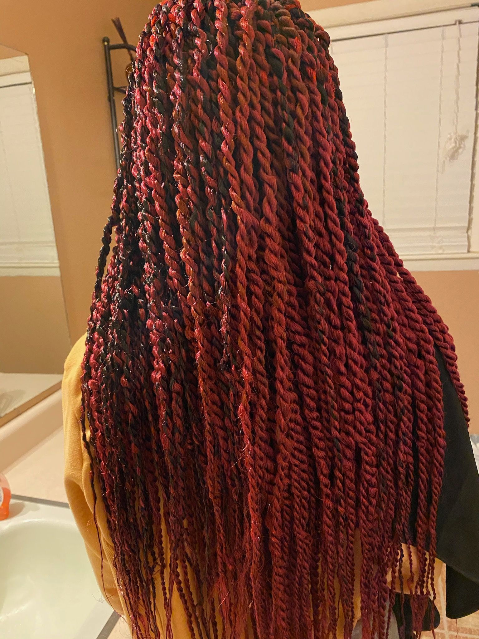 A Woman With Red Braids Is Standing In Front Of A Mirror In A Bathroom | Fayetteville, NC | Fatouisa African Braiding