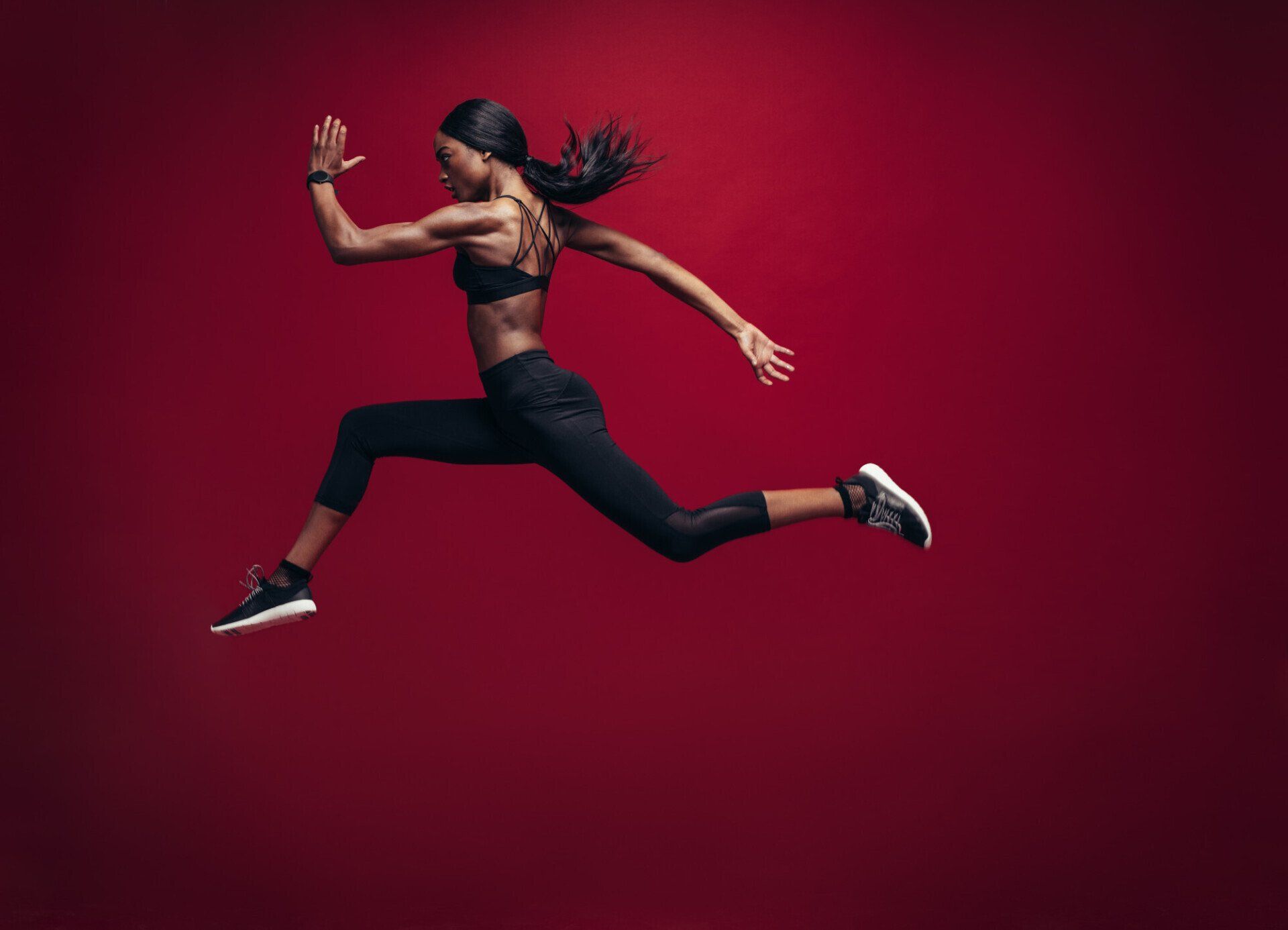 Athletic woman sprint jumping with dark red background