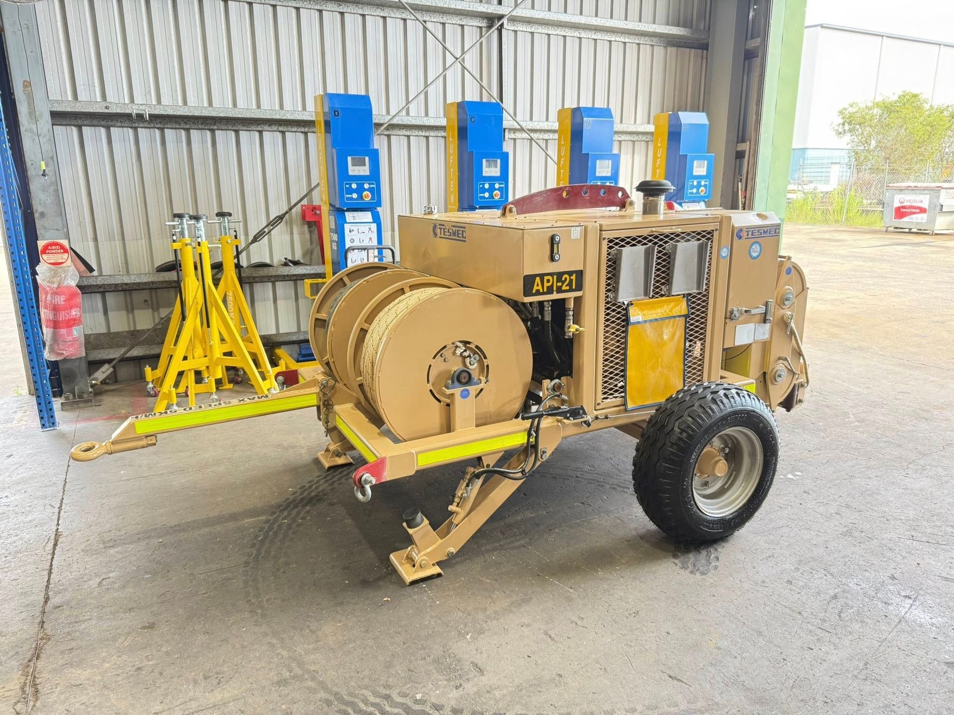 Yellow industrial machine on a trailer inside a warehouse, with blue equipment stands in the background