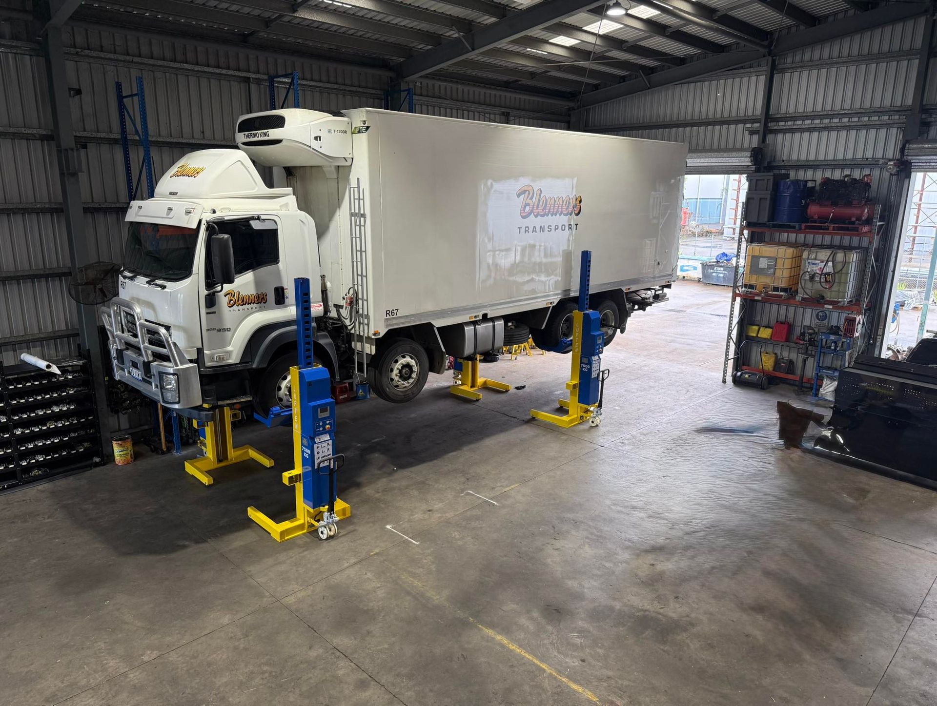 White box truck in a warehouse bay beside blue and yellow hydraulic lifts