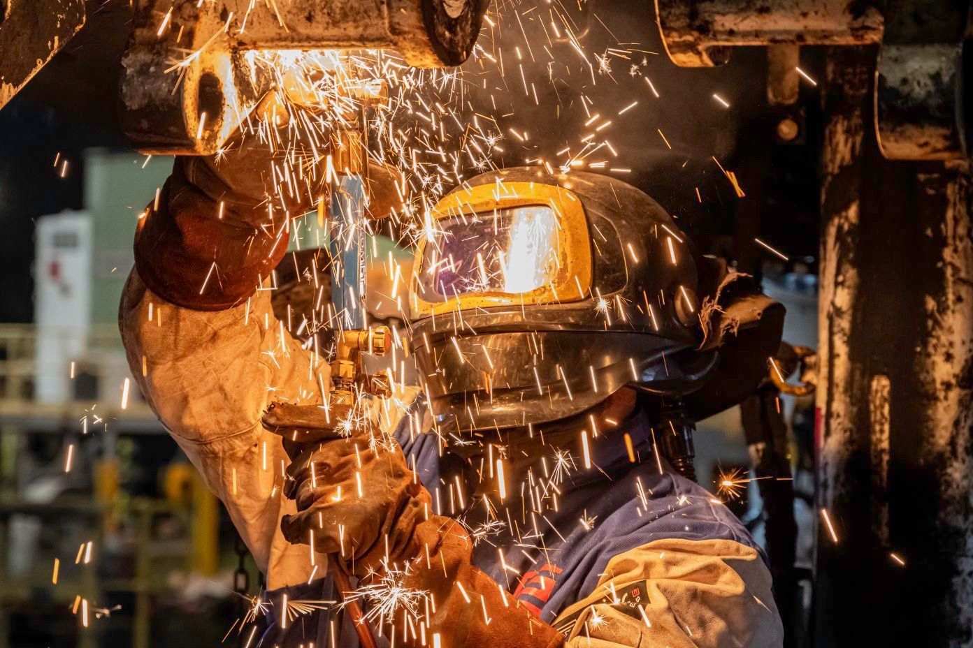Welder in protective gear sparks flying from metal in a workshop