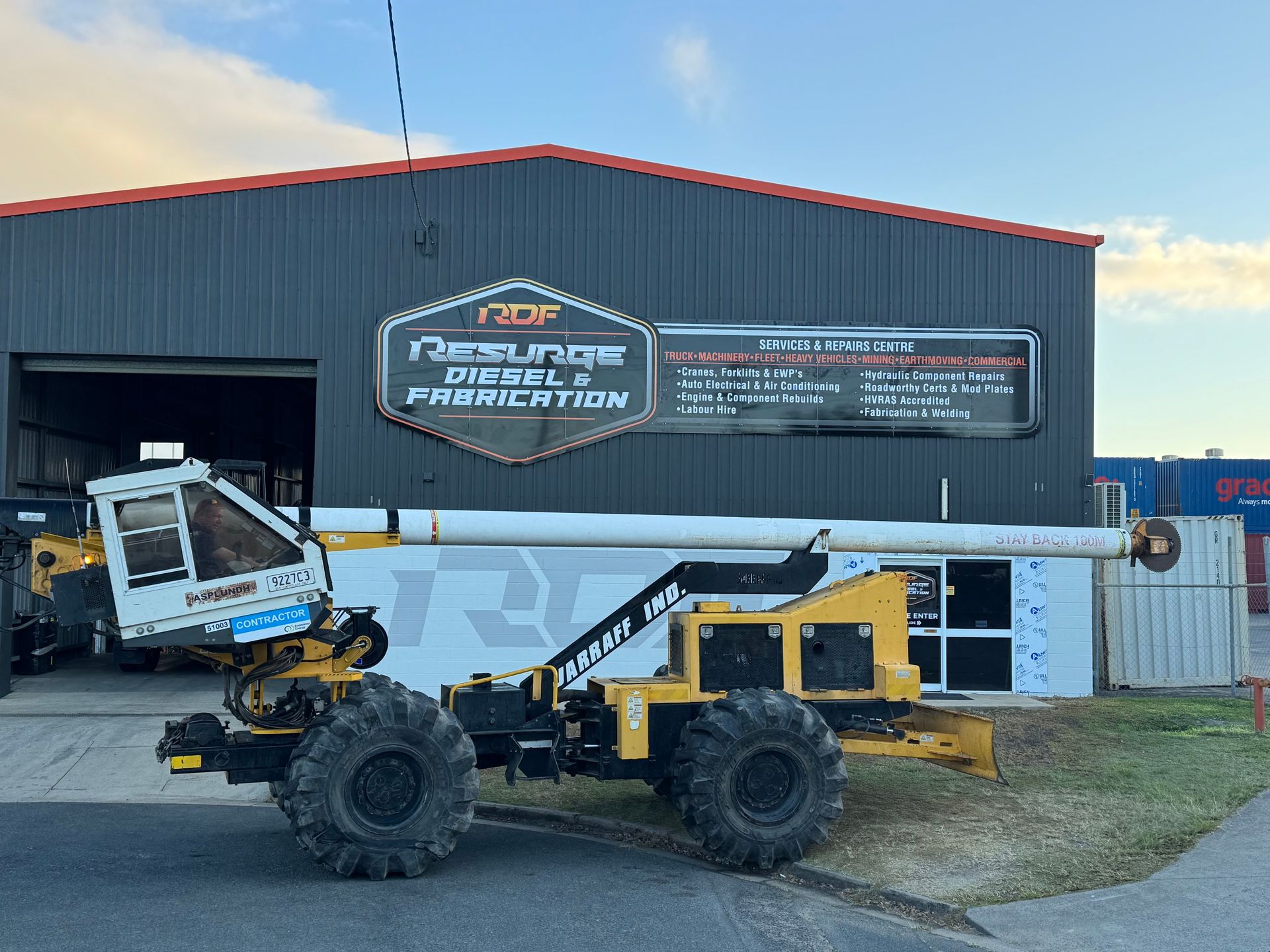 Yellow and black construction machine parked in front of a building with a sign that reads 