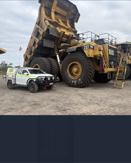 Massive mining haul truck beside a white pickup on a gravel lot, with a person on the truck ladder.
