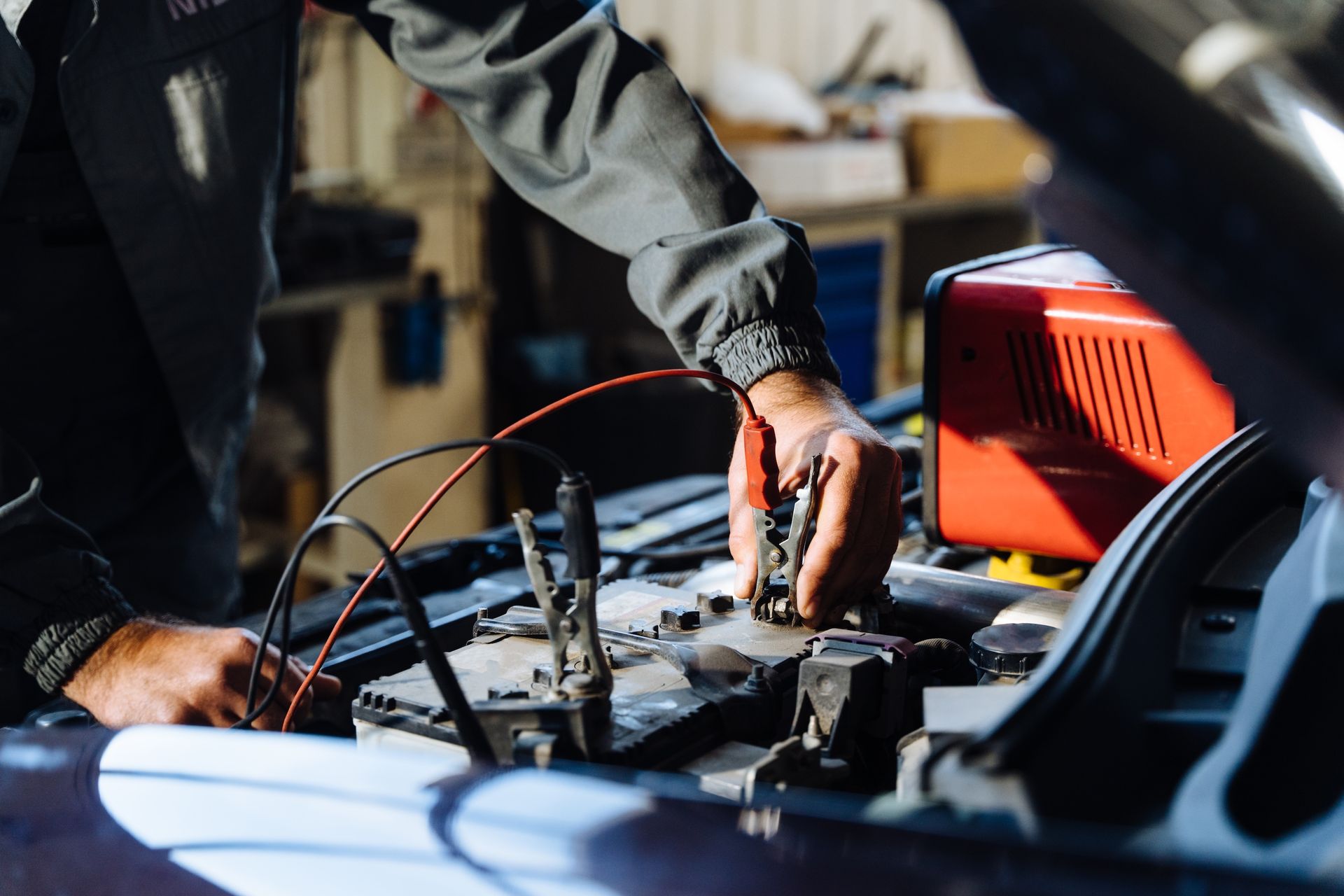 Mechanic Connecting Jumper Cables To A Car Battery In A Garagehands Connecting Blue Hose To Car Engine Bay Components — Resurge Diesel & Fabrication Pty Ltd In Balnagowan, QLD