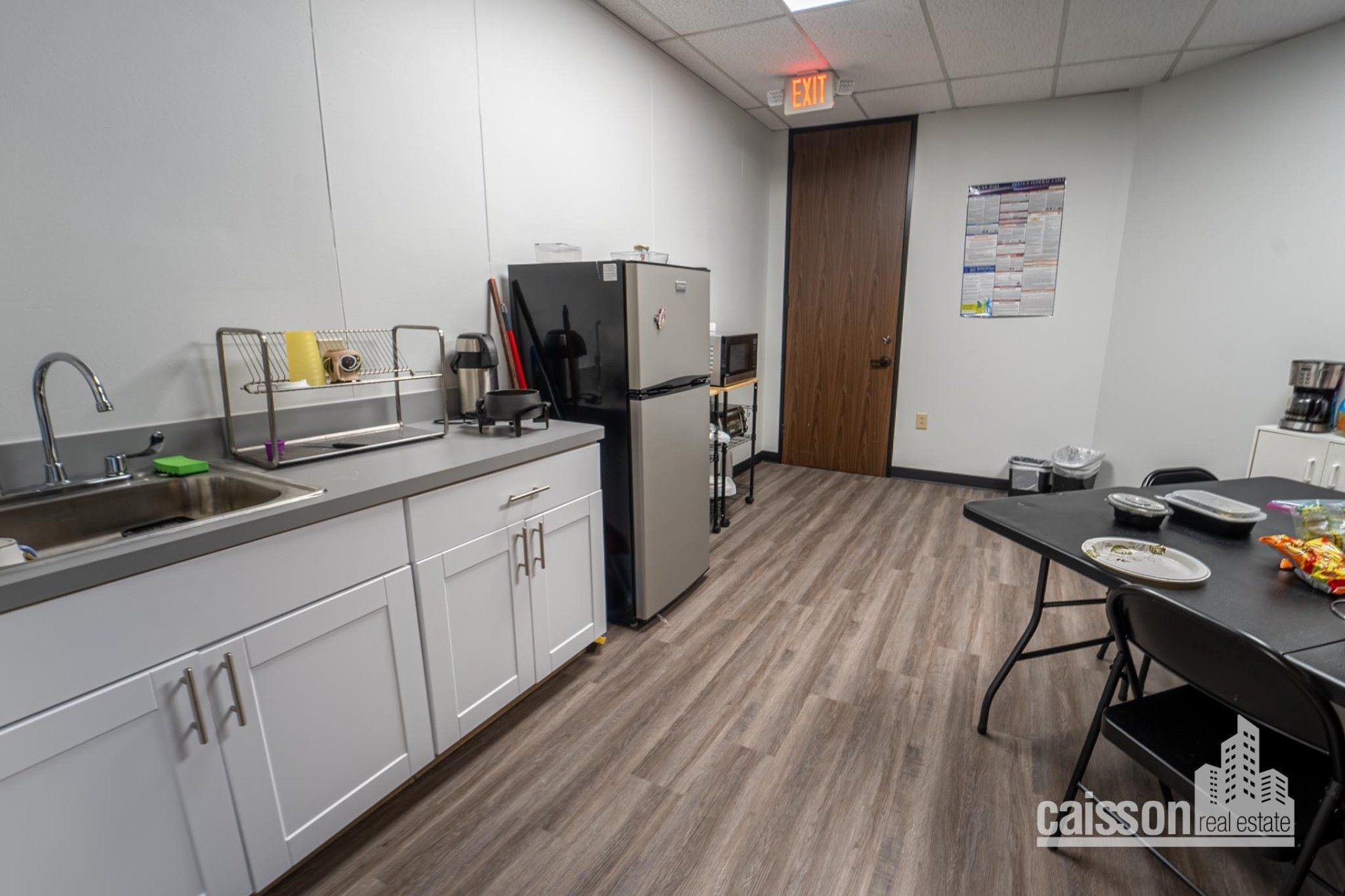 Interior view WestPark kitchenette with grey flooring, refrigerator, sink, and table with chairs.