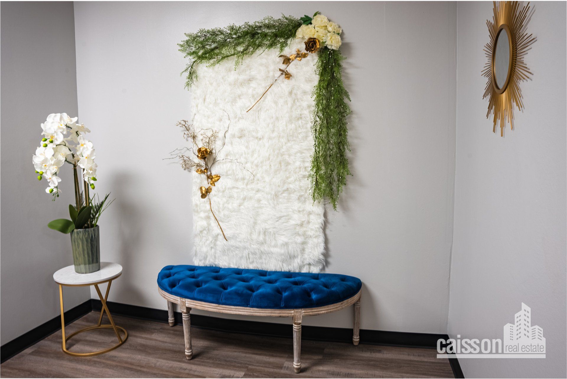 Interior view of lobby of a suite with grey flooring, blue bench, and flowers and white backdrop for photos.
