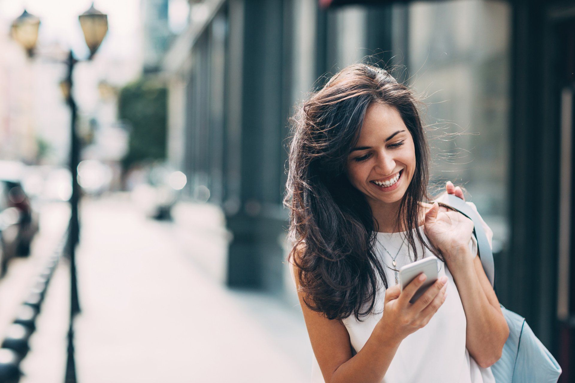 Happy woman shopping downtown, while carrying bag and looking at phone