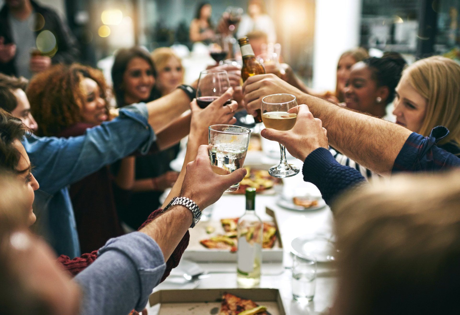 Happy group of friends at restaurant table and cheers with wine glasses.