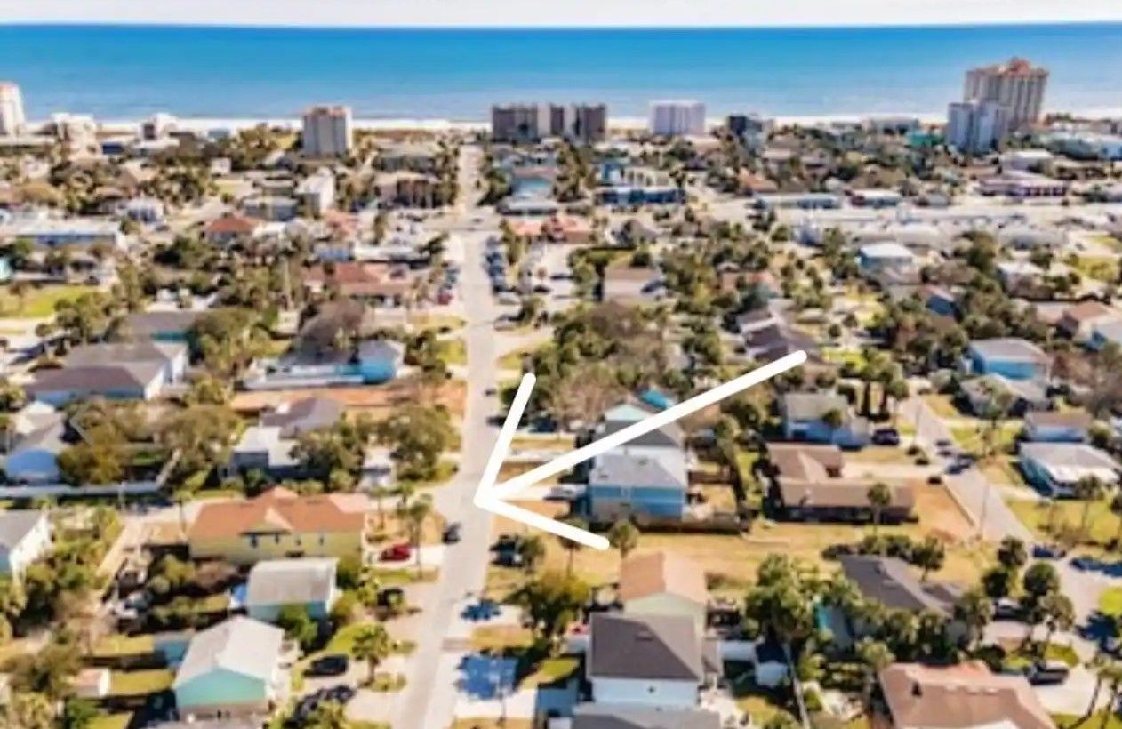 An aerial view of a residential area with a white arrow pointing to a house.