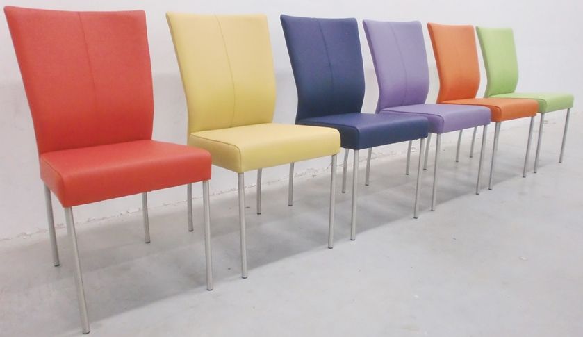 Een rij van zes moderne, gestoffeerde eetkamerstoelen in levendige kleuren: rood, geel, marineblauw, paars, oranje en lichtgroen.te bestellen bij stoelen-centrale.nl