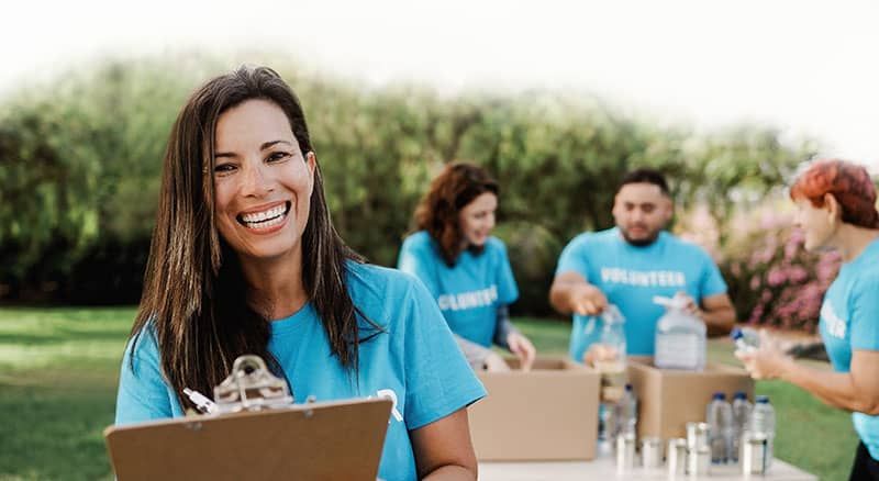 Smiling volunteers in blue shirts organize food donations outdoors at a community outreach event.