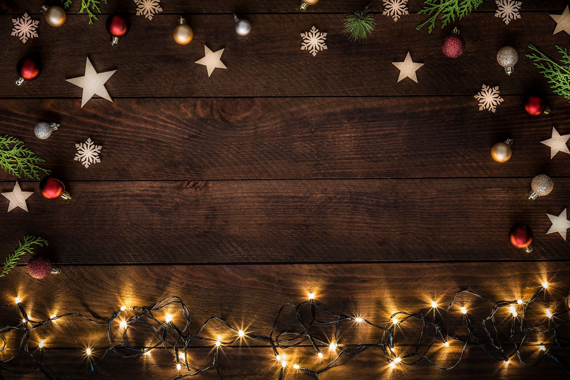 Wooden background with Christmas decorations: ornaments, stars, snowflakes, greenery, and string lights.