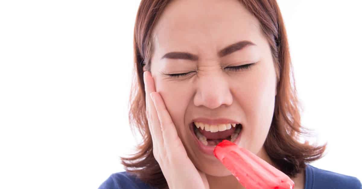 A woman is holding her face in pain while eating an ice cream cone.