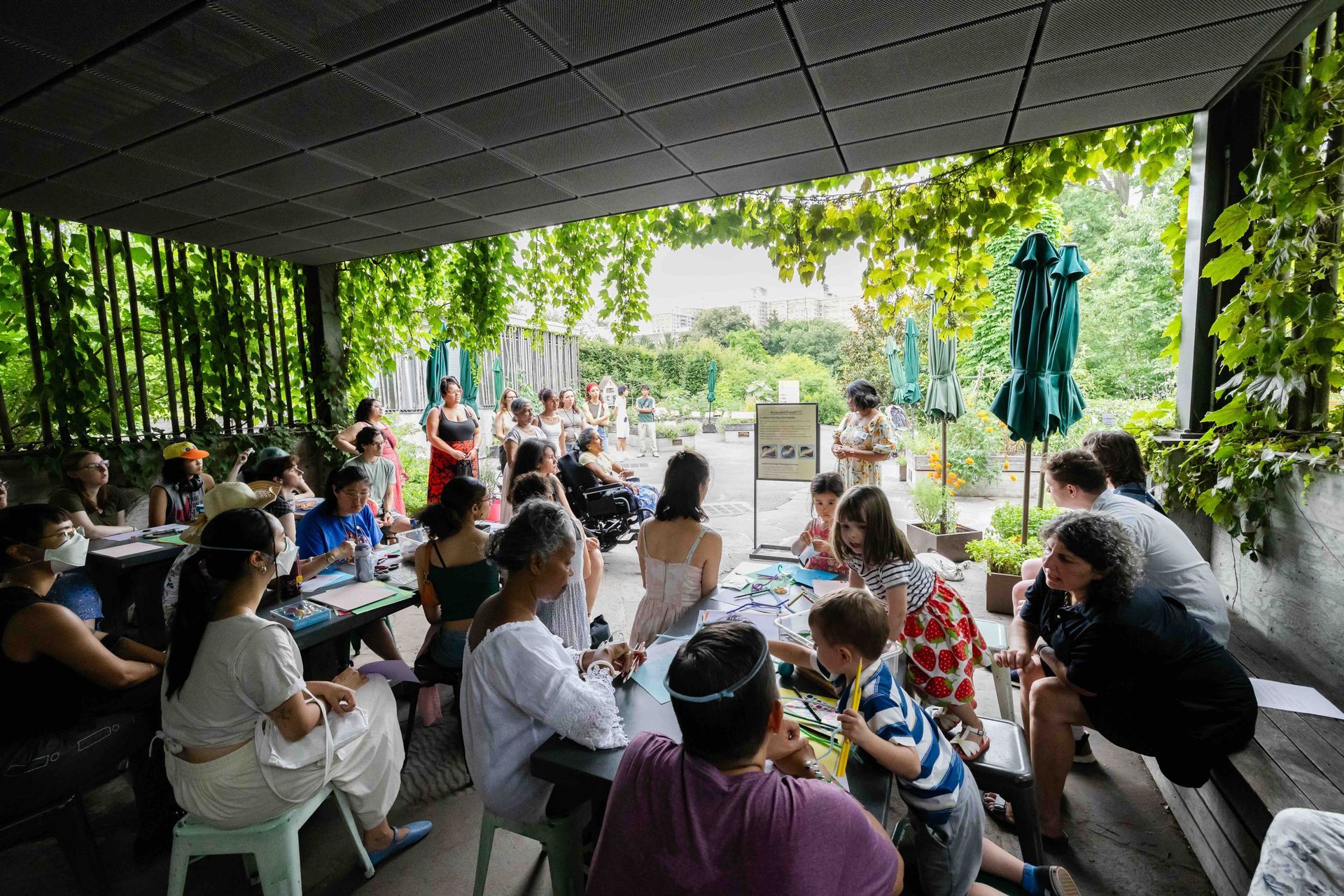 A photo taken of the group from the back of the program area showcasing many participants. Lakshmee and Annie are in front. The spot is beautifully adorned by lush green plants.