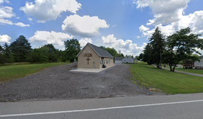 A small church is sitting in the middle of a grassy field next to a road. A small church is sitting in the middle of a grassy field next to a road.