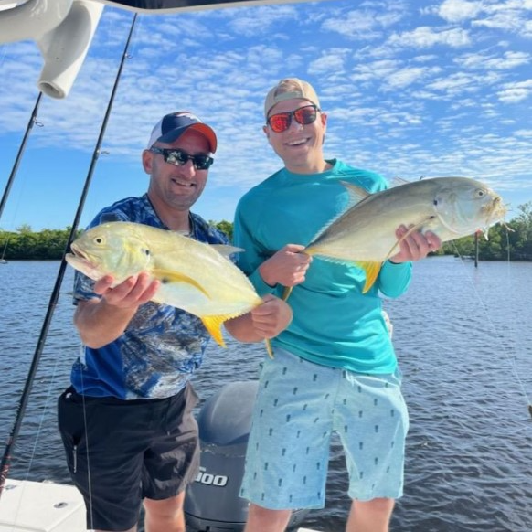 A speckled black and white grouper fish held by a scale on a boat with the ocean and sky in the background.