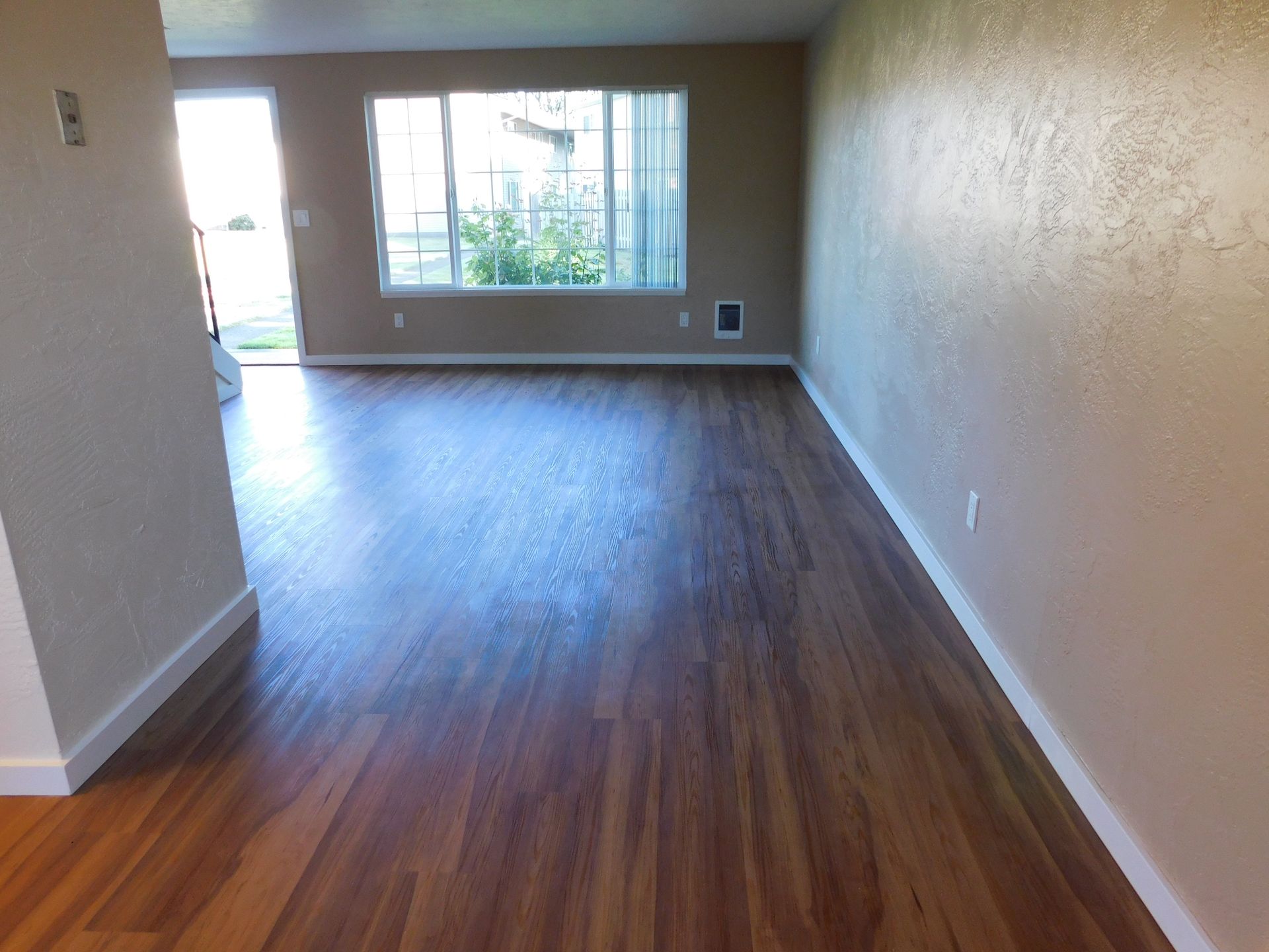 Empty living room with wood-look flooring, window, and door to the outside.