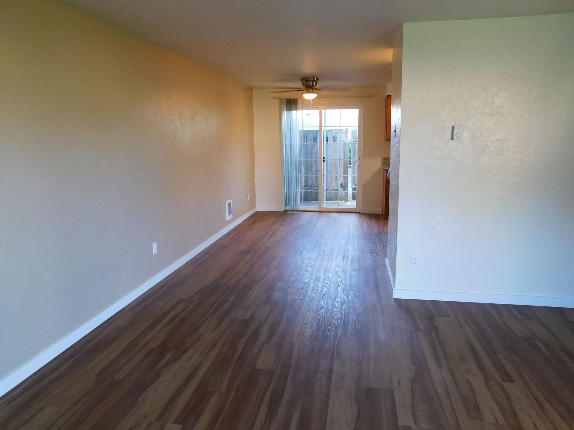 Living room with wood-look flooring, tan walls, sliding glass door leading to a patio, and a ceiling fan.