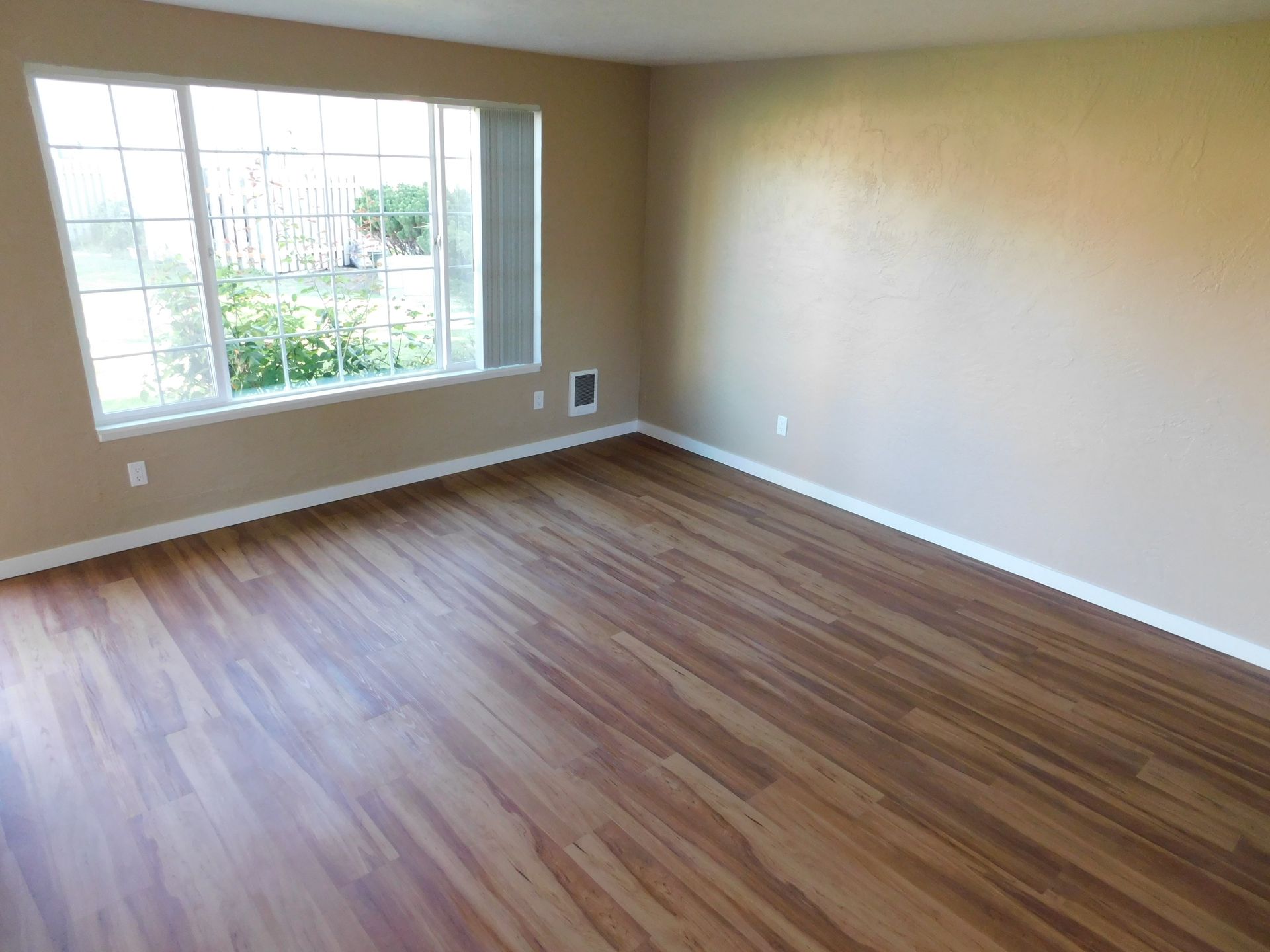 Empty room with wood-look flooring, tan walls, and a window overlooking greenery.