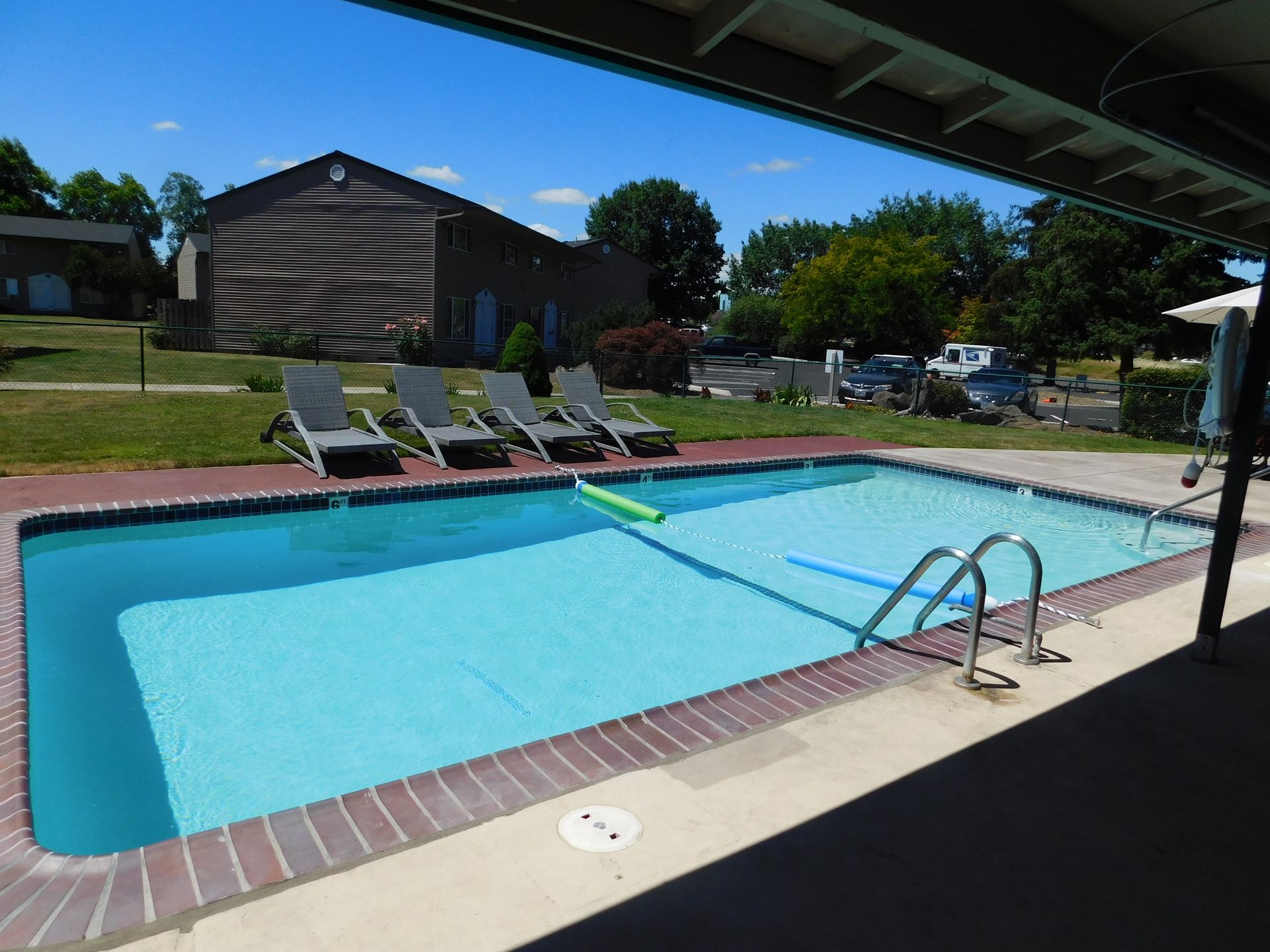 Swimming pool with lounge chairs, under a patio roof, on a sunny day.