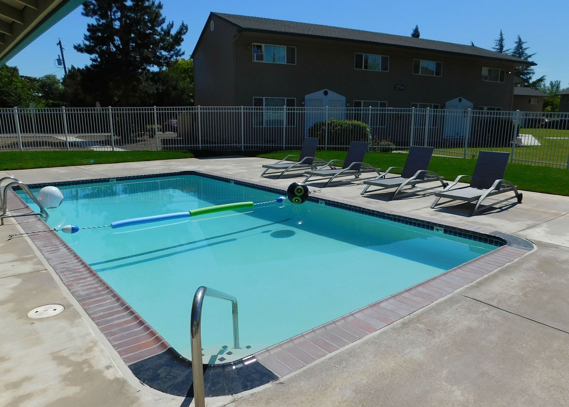 Rectangular pool with blue water, lounge chairs, and apartment building in the background.