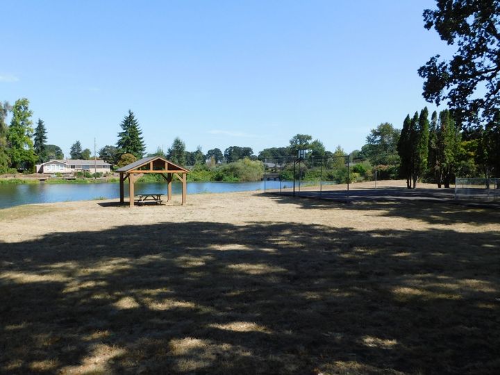 A lakeside park on a sunny day, with a gazebo, sand area, and dry grass.