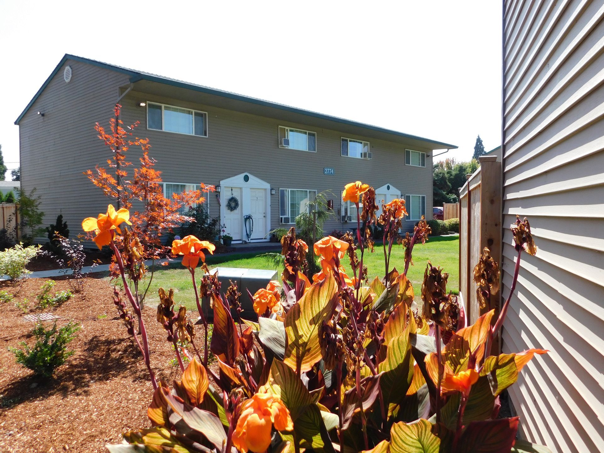 Two-story tan apartment building with orange flowers in front.