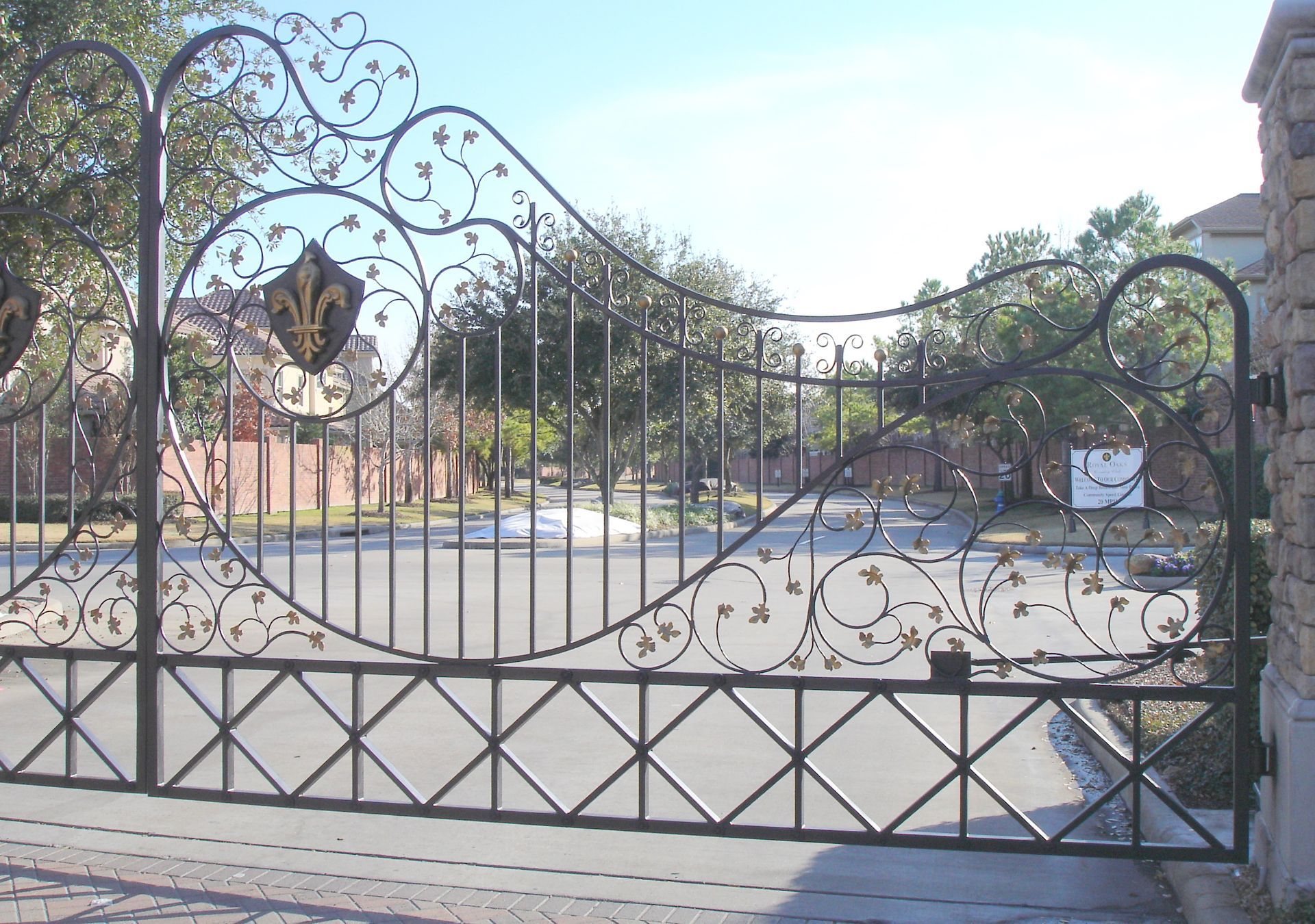 A wrought iron gate is open to a driveway